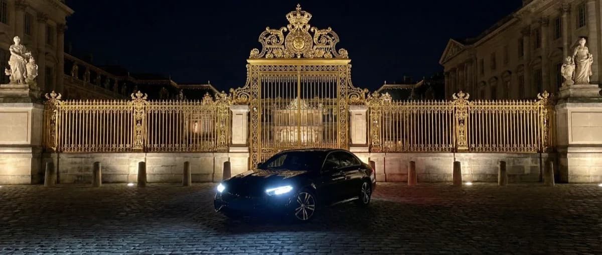 Voiture Mercedes privée devant les grilles dorées du Château de Versailles de nuit